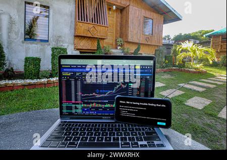 Manila, Philippinen. 26. März 2024: Binance-Website noch auf Laptop mit Telekommunikationsbetreiber Converge zugänglich, aber bereits von seinem Konkurrenten PLDT auf Smartphone verboten, vor dem traditionellen philippinischen Bambushaus 'Bahay Kubo'. Securities & Exchange Commission (SEC) ordnete philippinische Internetdienstanbieter an, den Kryptowährungsriesen Binance.com zu blockieren. Im Jahr 2017 hatte Duterte admin eine ähnliche Verbotsanordnung bezüglich populärer Websites für Erwachsene erlassen. Eine Zensur, die kein Ergebnis erwartet hatte: Seither ist die PH mit VPN immer in den Top-Ländern von Pornhub Stockfoto