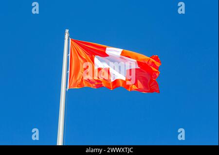 Die Flagge der Schweiz, die im Wind gegen einen blauen Himmel fliegt. Die Nationalflagge der Schweiz winkt im Himmel Stockfoto