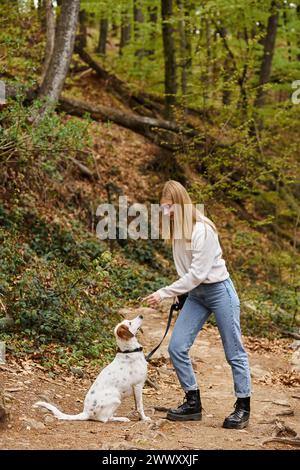 Happy Girl interagiert mit ihrem Haustier, das die Leine hält, bei Wanderausruhen mit Blick auf die Berge und den Wald Stockfoto