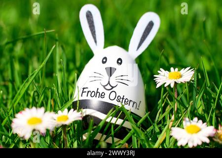 25. März 2024: Osterhasenei auf einer grünen Wiese mit Gänseblümchen und der Inschrift: Happy Easter Greeting. FOTOMONTAGE *** Osterhase EI in einer grünen Wiese mit Gänseblümchen und der Aufschrift: Frohe Ostern Ostergruß. FOTOMONTAGE Stockfoto