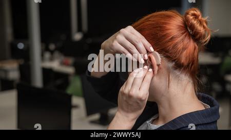 Kaukasische Frau, die im Büro ein Hörgerät auflegt. Stockfoto