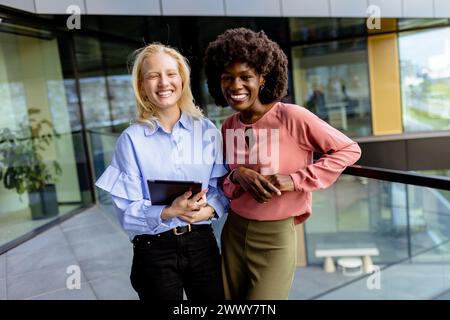 Zwei Frauen mit ähnlichen Merkmalen stehen nebeneinander, lächelnd, vor der großen Architektur. Stockfoto