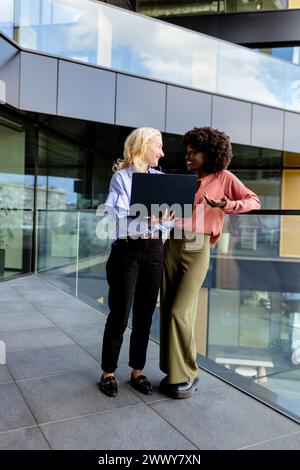 Zwei Frauen mit ähnlichen Merkmalen stehen nebeneinander, lächelnd, vor der großen Architektur. Stockfoto