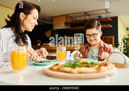 Positive Mutter isst Pizza und trinkt Saft mit ihrem niedlichen Sohn mit Down-Syndrom Stockfoto