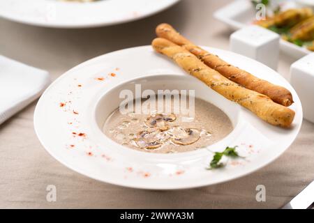 Champignonsuppe mit Brotstangen und frischen Pilzen auf weißem Teller. Sahnesuppe der Saison im Herbst Stockfoto