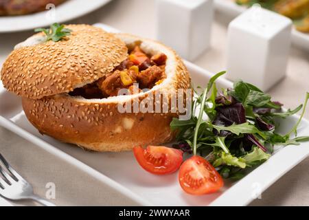 Fleischgulasch in einem Brotlaib, serviert auf einem weißen Teller in einem Restaurant. Traditionelle ungarische Küche Stockfoto