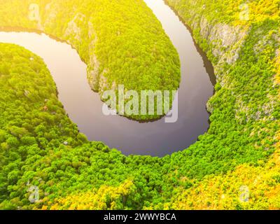 Ein Blick aus der Vogelperspektive auf einen ruhigen, gewundenen Fluss, der während der goldenen Stunde von üppigem Grün umgeben ist und die unberührte Schönheit der Natur zeigt. Stockfoto