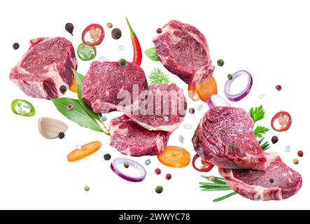 Rohe Rindersteaks, Kräuter und Gemüsestücke, die in der Luft schweben, auf weißem Hintergrund. Datei enthält Beschneidungspfad. Stockfoto