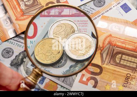 Geschäftlicher Hintergrund von weltberühmten Währungen - Papierscheine und Münzen in Euro und Dollar. Im Vordergrund hält die Hand eines Mannes eine Vergrößerung Stockfoto