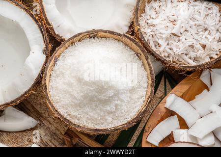 Frisch geöffnete Kokosnüsse zusammen mit Kokosscheiben, Flocken und Kokosblättern auf einem Holztisch. Schöner Hintergrund für Ihre Projekte. Stockfoto