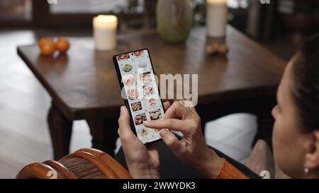 Lebensmittel mit einem Smartphone zu Hause bestellen. Eine Frau wählt Sushi-Sets im Internetmenü eines japanischen Restaurants mit einer Anwendung auf einem Smartphon aus Stockfoto