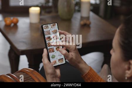 Lebensmittel mit einem Smartphone zu Hause bestellen. Eine Frau wählt Sushi-Sets im Internetmenü eines japanischen Restaurants mit einer Anwendung auf einem Smartphon aus Stockfoto