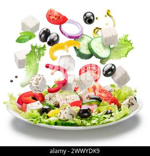 Frisches Gemüse und Fetakäse fallen isoliert in die weiße Platte. Datei enthält Beschneidungspfade. Stockfoto