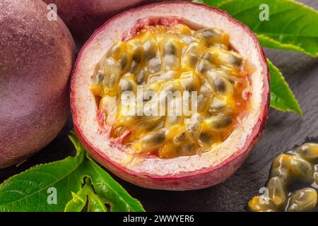 Dunkelviolette Passionsfrüchte und die Hälfte der Maracuya-Frucht isoliert auf Schiefergraphit-grauem Hintergrund. Stockfoto