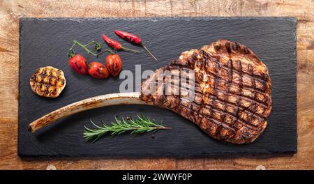 Gegrilltes, köstliches Tomahawk-Steak und einige Gewürze auf einem Servierteller aus schwarzem Schiefer. Flache Lagen. Stockfoto