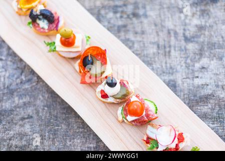 Fingerfood, verschiedene Canapes mit Gemüse, Schinken, Speck, Käse und Oliven auf Holztisch. Stockfoto