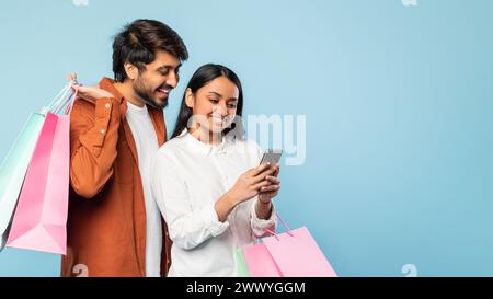 indische Paare, die online in Anwendung am Telefon einkaufen, blauer Hintergrund Stockfoto