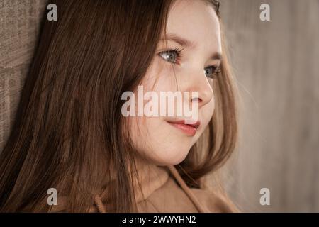 Süßes kleines Mädchen mit grauen Augen, die in die Ferne schauen. Ich dachte an etwas angenehmes. Nahaufnahme Porträt. Beige Töne. Horizontales Foto. Stockfoto