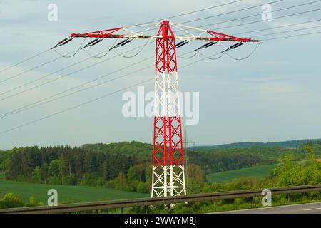 Ein rot-weißer Stromanschluss steht am Straßenrand und dient als Stütze für elektrische Leitungen. Stockfoto