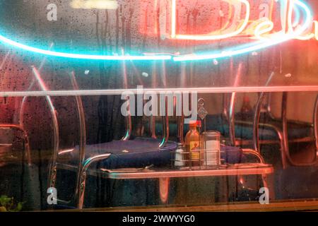Blick durch das nasse, regnerische nebelige Fenster eines geschlossenen Diner oder Delis mit aufgeklappten Stühlen auf den Tischen Stockfoto