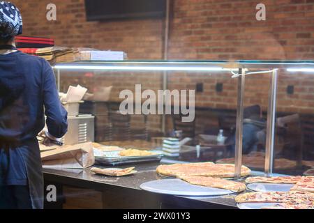 Arbeitende Frau in einer Pizzeria, die eine Vielzahl frischer Pizzen in einer rustikalen und warmen Atmosphäre zubereitet Stockfoto