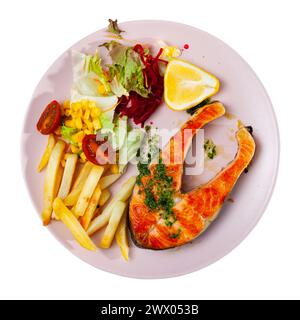 Lachs wird mit Pesto abgeschmeckt und mit Pommes frites, Salat mit frischem Gemüse und Crackern garniert Stockfoto