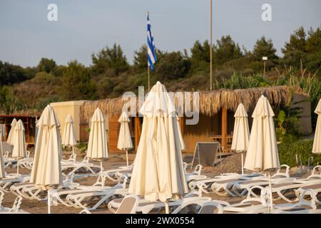 Zusammenklappbare Sonnenschirme und Sonnenliegen am Strand in Rhodos, Griechenland Stockfoto