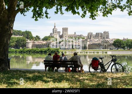 Avignon, Provence, Frankreich - 26. Juni 2021: Gruppe von Freunden mittleren Alters, die auf einer Bank vor der Rhone sitzen und einen wunderschönen Blick auf Avignon haben Stockfoto