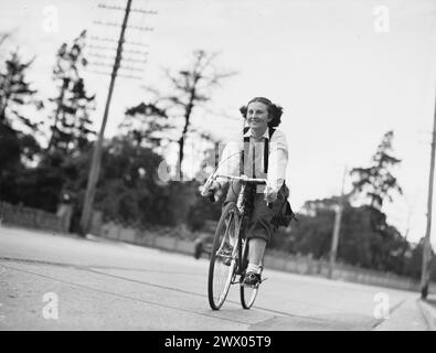 Ein junges Mädchen, das Fahrrad fährt und lächelt. Vintage-Fotografie während des Benzinrationings in Sydney, Australien, 2. Weltkrieg. Juli 1940. Fotorechte: A. Grimes Stockfoto