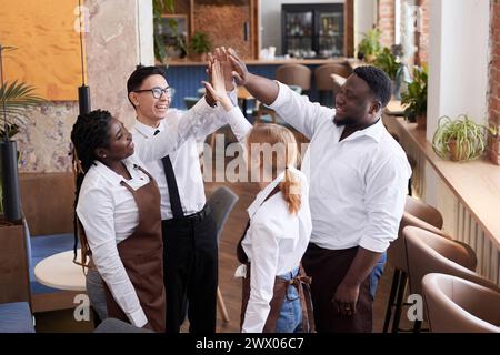 Blick aus einem hohen Winkel auf junge, erfolgreiche Multi-ethnische Kellner, die High Five bei der Arbeit in einem modernen Restaurant machen Stockfoto