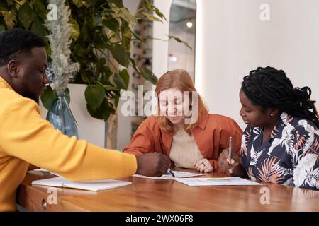 Afroamerikanische und kaukasische Männer und Frauen in stilvoller Freizeitkleidung, die Geschäftstreffen in einem modernen Restaurant veranstalten Stockfoto