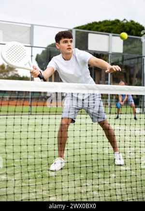 Junger Europäer, der im Herbst beim Tennisspiel hinter dem Netz Padel spielt Stockfoto