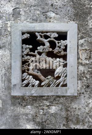 Ein Steinschnitzerschnitt schafft ein kleines, dekoratives Fenster in einer Felsmauer in der antiken Stadt Xidi. Stockfoto