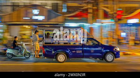 Ein blauer Songthaew fährt nachts durch eine geschäftige Straße mit verschwommenem Langzeitlicht in Pattaya, Thailand Stockfoto