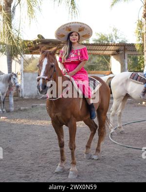 Mexikanische Frau mit traditionellem Kleid und charro-Hut zu Pferd. Cinco de Mayo-Feier. Stockfoto