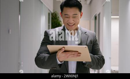 Glücklicher asiatischer ethnischer Mann mittleren Alters chinesischer koreanischer Geschäftsmann lächelnder Geschäftsgeber Verwenden Sie ein digitales Tablet im Büro Flur Lobby männlicher Unternehmer Stockfoto