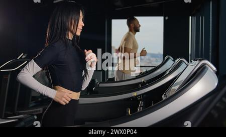 Motivierte Sportler Läufer Cardio-Training auf Laufbändern aktives Workout im Fitnessclub Frauen und Mann Paar Athleten laufen Sprint-Jog in der Dunkelheit Stockfoto