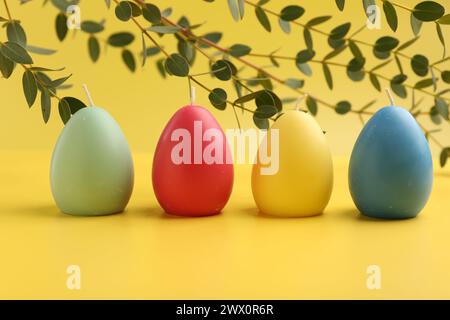 Bunte Kerzen und Blätter in Eierform auf gelbem Hintergrund. Osterdekor Stockfoto