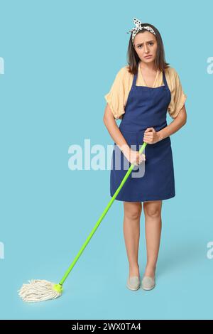 Porträt müder junger Hausfrau in Schürze mit Wischtuch auf blauem Hintergrund Stockfoto