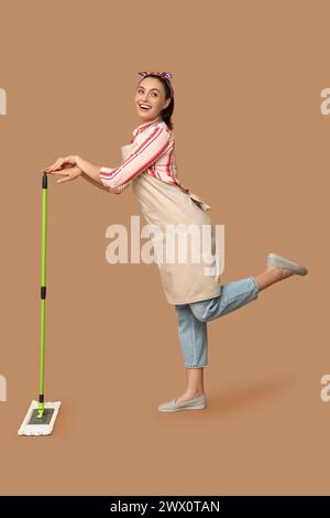 Porträt einer glücklichen jungen Hausfrau in Schürze mit Wischtuch auf braunem Hintergrund Stockfoto