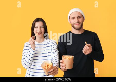 Schönes junges Paar mit Pommes frites auf gelbem Hintergrund Stockfoto