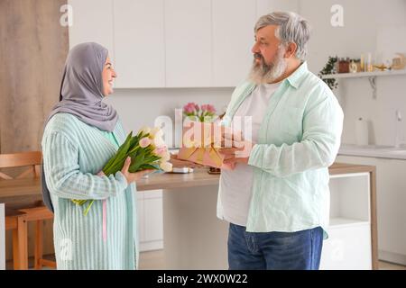 Reifer muslimischer Mann begrüßt seine Frau mit Geschenk in der Küche. Ramadan-Feier Stockfoto