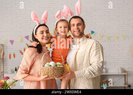 Glückliche Familie in Hasenohren, die zu Hause einen Korb mit Ostereiern hält Stockfoto