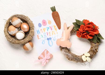 Grußkarte mit Text HAPPY EASTER, Eggs, Spielzeughase, Kranz und Geschenkbox auf weißem Hintergrund Stockfoto