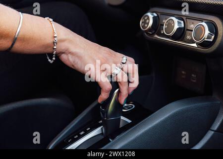 Nahaufnahme der Hand einer Frau, die einen Automatikgetriebehebel im Fahrzeug hält. Selektiver Fokus auf die weibliche Hand. Stockfoto