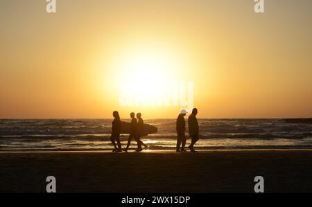 Surfer laufen am Strand bei Sonnenuntergang in Tel-Aviv, Israel. Stockfoto