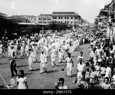 Originalunterschrift: 'Blechband führt eine Prozession der Menschen von Singapur bei der Siegesfeier an, um ihre Freude über die Landung der Empire Forces zu demonstrieren, um Singapur zu besetzen nach 3,5 Jahren japanischer Herrschaft hielten die Menschen eine Feier ab. Die Band ist die Royal Marines." CA. September 1945 Stockfoto