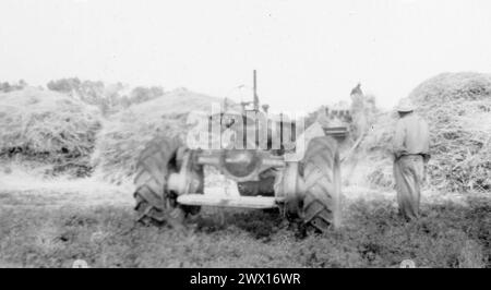 Landwirt steht neben einem Traktor mit Heuballen im Hintergrund ca. 1930er oder 1940er Jahre Stockfoto