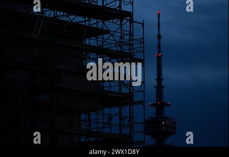 München, Deutschland. März 2024. Gerüste stehen auf einer Baustelle auf der Hülle eines neuen Gebäudes. Der Olympiaturm ist im Hintergrund zu sehen. Quelle: Sven Hoppe/dpa/Alamy Live News Stockfoto