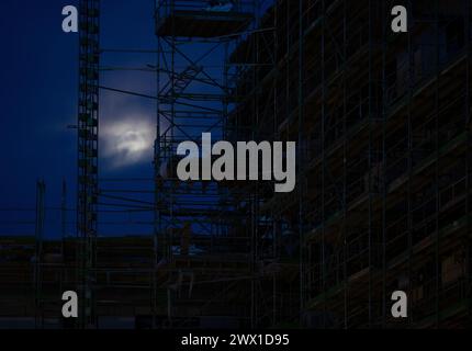 München, Deutschland. März 2024. Gerüste stehen auf einer Baustelle auf der Hülle eines neuen Gebäudes. Der Mond ist im Hintergrund zu sehen. Quelle: Sven Hoppe/dpa/Alamy Live News Stockfoto